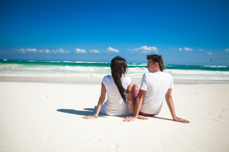 Back view of young couple in love sitting at tropical white beachの写真素材