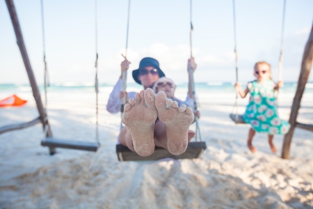 young mother and her cute daughter swinging on a swing at the beachの写真素材