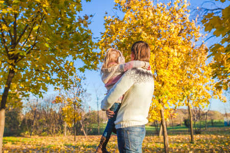 Back view of Little girl with happy father having fun in autumn park on a sunny dayの写真素材
