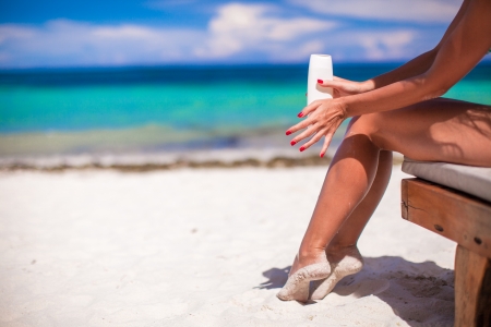 Young woman apply cream on her smooth tanned legs on tropical beacの写真素材