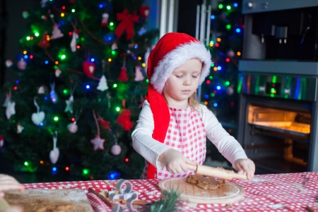 Little girl in Santa hat with rolling pin baking gingerbread cookiesの写真素材