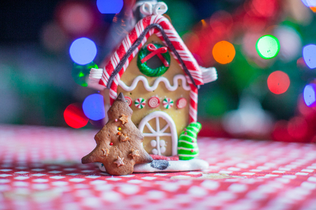 Gingerbread house decorated by sweet candies on a background of bright Christmas tree with garlandの写真素材