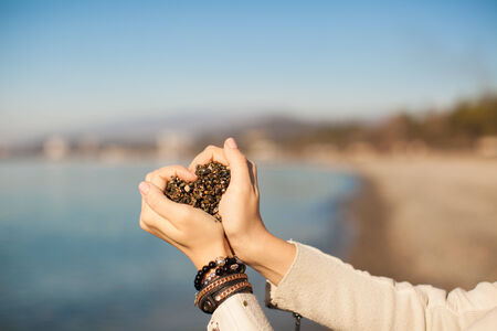 Woman hands holding small stones form heart shape background the seaの写真素材