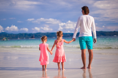 Back view of two little girls and young father on tropical white beachの写真素材