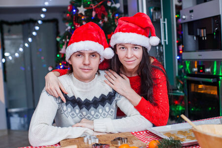 Portrait of young happy couple baking Christmas cakes at home in Santa hatの写真素材