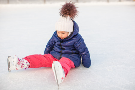 Little adorable girl sitting on the ice with skates after the fallの写真素材