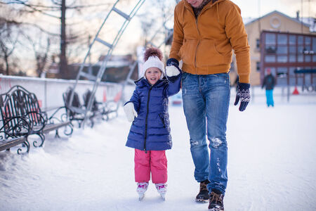Closeup of adorable little girl with young dad on skating rinkの写真素材