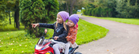 Adorable little girls riding on kid's bike in the green parkの写真素材