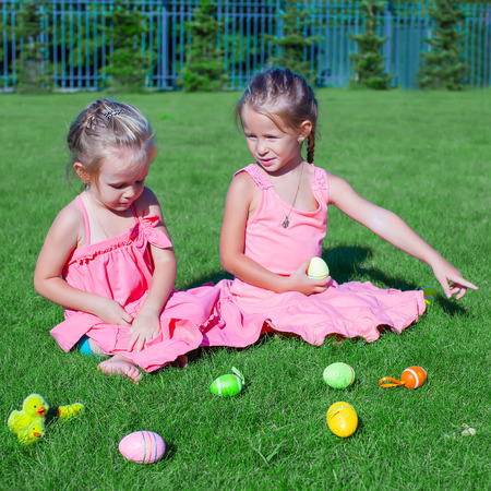 Two adorable little girls playing with Easter Eggs on green grassの写真素材