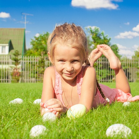 Portrait of little cute girl playing with white Easter eggs on green grassの写真素材