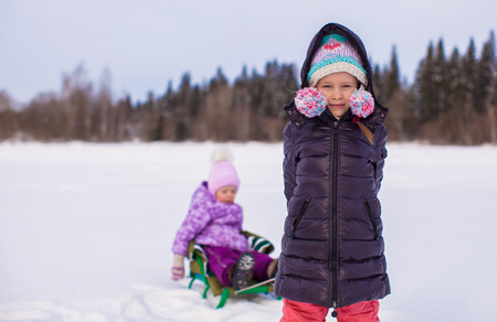 Adorable little happy girl sledding her sister