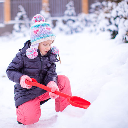 Little girl play with snow shoveling on a winter dayの写真素材