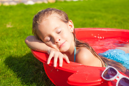Portrait of relaxing adorable little girl enjoying her vacation in small pool outdoorの写真素材