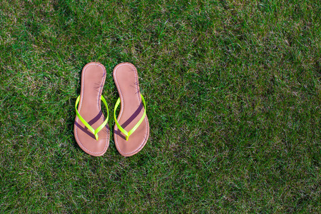 Closeup of bright flip flops and legs on green grassの写真素材