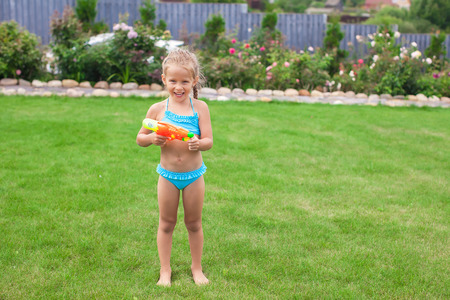 Little adorable girl playing with water gun outdoor in sunny summer dayの写真素材
