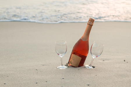 Bottle of red wine and two glasses on the white sandy beachの写真素材