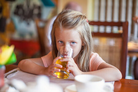 Cute little girl having breakfast and drinking fruit juiceの写真素材