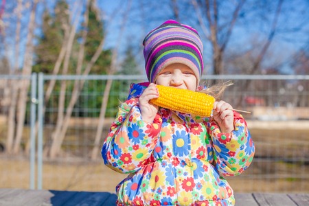 Little girl eating corn in the park on a warm spring day