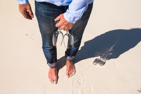 Closeup of two glasses in hand at man walking barefoot on the beach