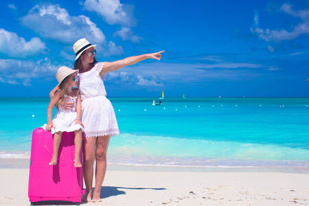 Young mother and her daughter with luggage on tropical white beachの写真素材