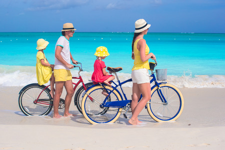 Young family of four riding bicycles on a tropical white sand beach