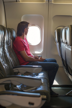 Young man looking in window on board of an airplaneの写真素材