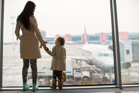 Mother and little daughter looking out the window at the airport terminal