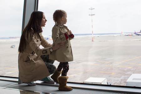 Mother and little daughter looking out the window at the airport terminalの写真素材