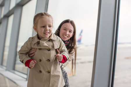 Mother and little daughter looking out the window at the airport terminalの写真素材