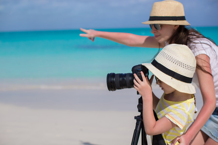 Little girl with camera walking with young mother at tropical beachの写真素材