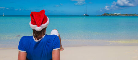 Back view of young man in santa hat on tropical beachの写真素材