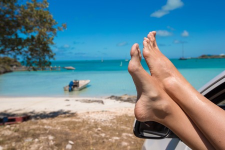 Female feet from the window of a car on a background of tropical beachの写真素材