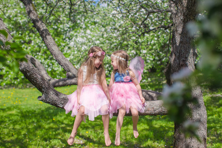 Little adorable girls with butterfly wings under blossoming apple treeの写真素材