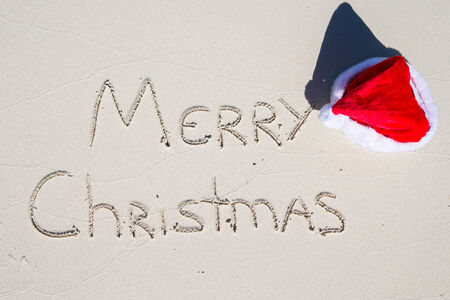 Merry Christmas written on tropical beach white sand with red xmas hatの写真素材