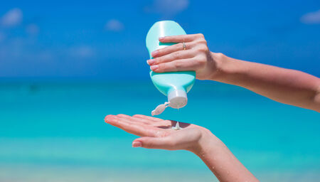 Woman hands putting sunscreen from a suncream bottleの写真素材