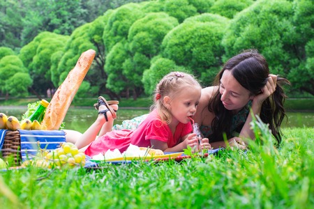 Cute little girl and happy mom picnicking in the park outdoorの写真素材