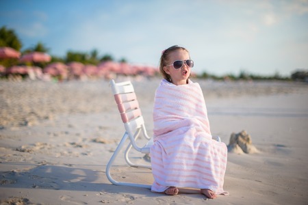 Adorable little girl covered with towel sitting on beach chairの写真素材