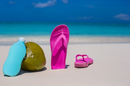 Flip flops, coconut and suncream on white sandの写真素材