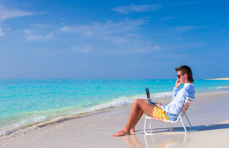 Young man working on laptop at tropical beachの写真素材