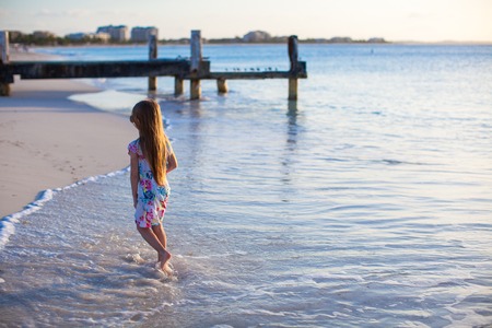 Adorable little girl walking at white tropical beach on sunsetの写真素材