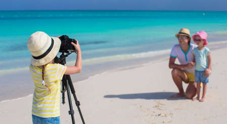 Little girl photographing her dad and sister on the beachの写真素材