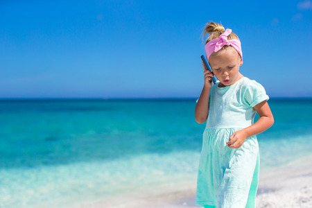 Little adorable girl talking at phone during beach vacationの写真素材