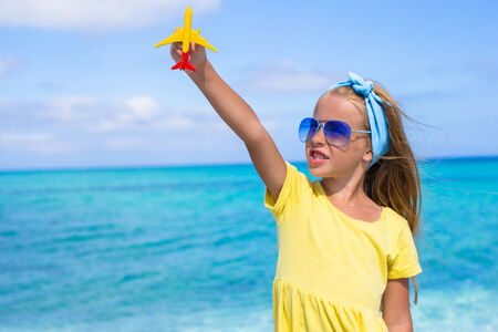 Happy little girl with toy airplane in hands on white sandy beachの写真素材