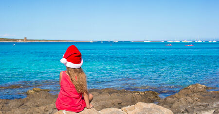 Back view of cute little girl in Santa hat on the beachの写真素材
