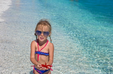 Little adorable girl with sea star at the tropical beachの写真素材