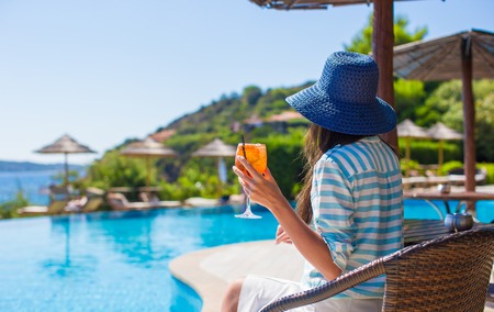Back view of young woman sitting in tropical cafe near swimming poolの写真素材