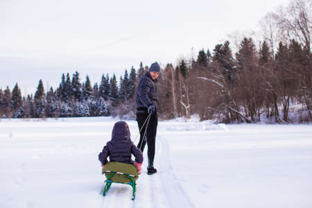 Young dad rolls his child on sledge in winter sunny dayの写真素材