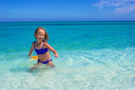 Adorable little girl have fun in shallow water at tropical beachの写真素材