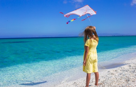 Little happy girl playing with flying kite on tropical beachの写真素材