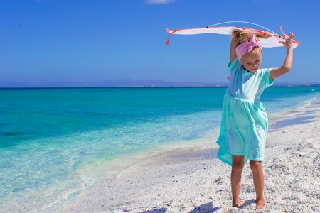 Little happy girl playing with flying kite on tropical beachの写真素材